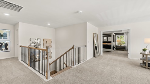 Butner Estates community model home second floor loft area with light carpet and multiple windows for natural light used as a living space