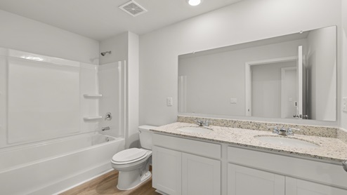 A bathroom with tub shower, double sink vanity, and a toilet.