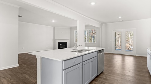 Interior kitchen with center island and light grey cabinets open to living area