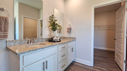 Dual sink vanity with granite countertop and access to walk-in closet.