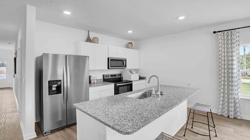 Kitchen peninsula with white cabinets, granite countertops and stainless-steel appliances.