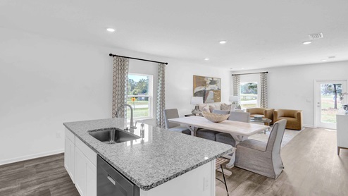 Kitchen peninsula with white cabinets and granite countertops overlooking the dining and living areas.