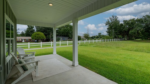 Covered back porch with two columns overlooking large yard.