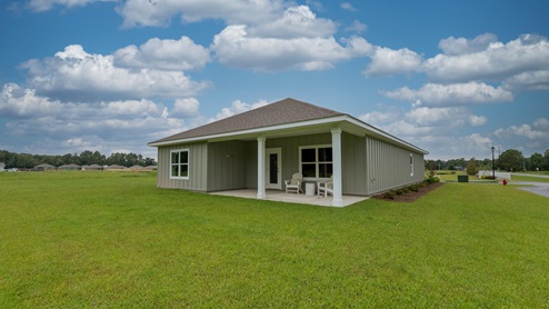Covered back porch with neutral-green board and batten, two columns, and a spacious backyard.