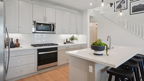 Modern kitchen with light grey cabinets quartz countertops and stainless steel appliances