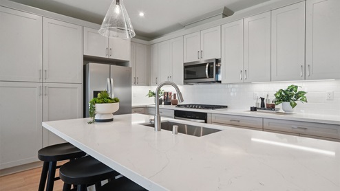 Modern kitchen with light grey cabinets quartz countertops and stainless steel appliances