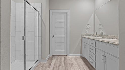 Attached primary bathroom with double sink vanity and tiled walk-in shower