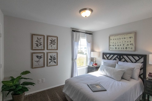 Creekside Hills model home secondary bedroom with queen bed and light-colored decorative pieces.