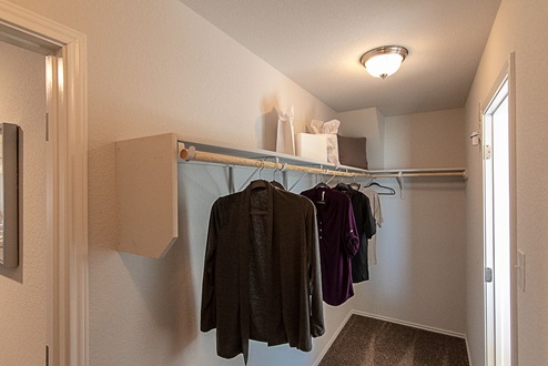 Creekside Hills model home primary closet with a few clothing items hung on hanging rods.
