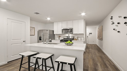 Open kitchen with an island, stainless steel appliances, white cabinets, white walls, and vinyl wood flooring.