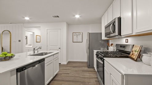 Open kitchen with an island, stainless steel appliances, white cabinets, white walls, and vinyl wood flooring.