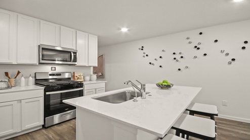 Open kitchen with an island, stainless steel appliances, white cabinets, white walls, and vinyl wood flooring.