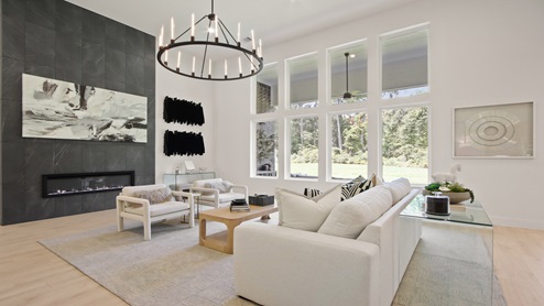 Open living room with large windows, artificial fireplace with stone, white walls, and light vinyl wood flooring.