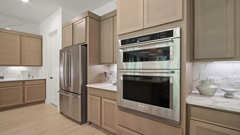 Large open kitchen with an island, upgraded stainless steel appliances, light stained cabinets, white and gray quartz countertops, white walls, and light vinyl wood flooring.