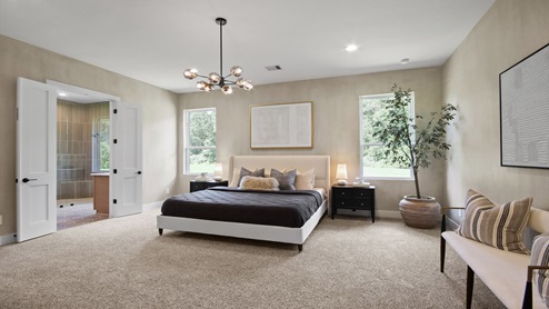 Primary bedroom with windows, white walls, and light carpet.