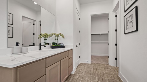 Primary bathroom with two separate sinks and vanities, light stained cabinets, white and gray quartz countertops, walk-in super shower, white walls, and light vinyl wood flooring.