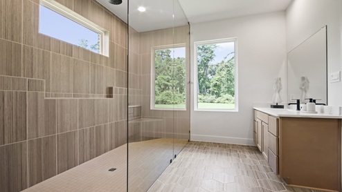 Primary bathroom with two separate sinks and vanities, light stained cabinets, white and gray quartz countertops, walk-in super shower, white walls, and light vinyl wood flooring.