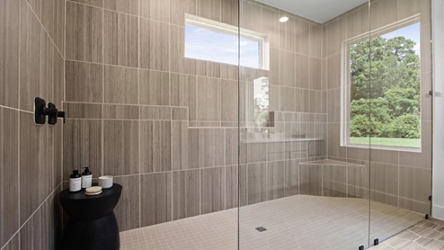 Primary bathroom with two separate sinks and vanities, light stained cabinets, white and gray quartz countertops, walk-in super shower, white walls, and light vinyl wood flooring.