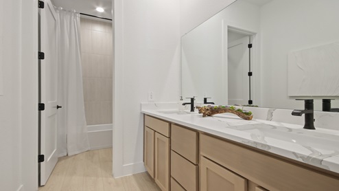 Secondary bathroom with a sink, white and gray quartz countertops, shower and tub combo, light stained cabinets, white walls, and light vinyl wood flooring.