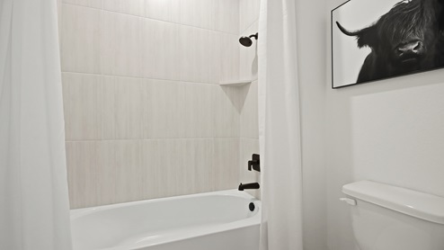 Secondary bathroom with a sink, white and gray quartz countertops, shower and tub combo, light stained cabinets, white walls, and light vinyl wood flooring.