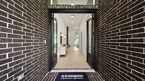 Entry hallway with brick, double doors, white walls, and light vinyl wood flooring.