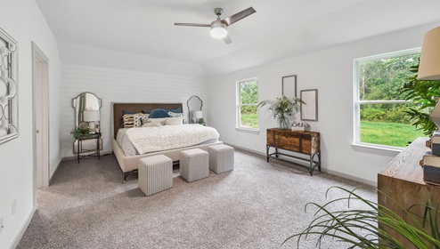 Holly Trails model home primary bedroom with a king bed and carpet flooring.