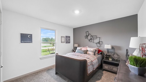 Holly Trails model home secondary bedroom with a full-size bed and carpet flooring.