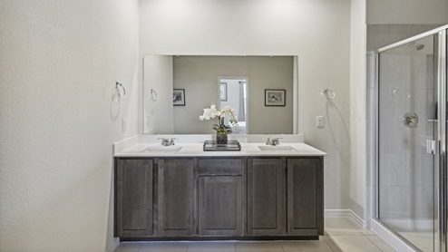 Primary bathroom with long vanity with brown cabinets and a walk-in shower