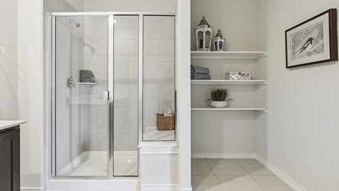 Primary bathroom with long vanity with brown cabinets and a walk-in shower and shelving