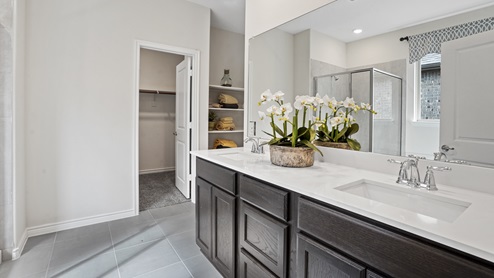 large primary bathroom with elongated vanity with white counter brown cabinets and large mirror