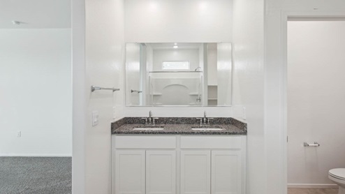 Modern primary bathroom with double vanities, granite countertops with a walk-in shower and a walk-in closet.