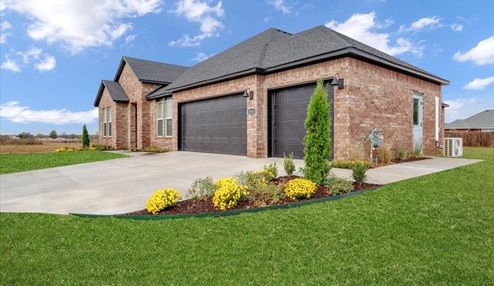 Exterior view of a modern brick house with a spacious driveway and well-maintained green lawn, featuring a dark roof and a three-car garage with matching black doors.
