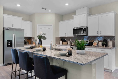Kitchen with island seating, granite counters, spacous pantry and stainless steel appliances.
