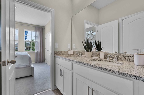 Modern bathroom with double vanity, large wall mirror, cabinets and granite countertops showing access to master bedroom.