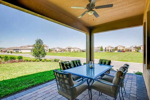 Covered rear of home with view of grassed backyard, table and sitting and slider doors.