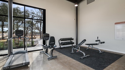Bulverde Texas DR Horton Homes Copper Canyon New Construction Homes indoor fitness center with stained concrete flooring floor to ceiling windows for plenty of natural lighting treadmill stationary bike rack of free weights and benches