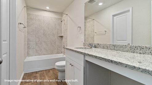 primary ensuite bathroom with tiled tub and shower combo, toilet, and single vanity sink with plenty of counter space