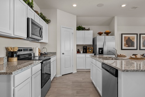Rockbridge Model Home open-concept kitchen with white cabinetry, granite countertops and backsplash, stainless-steel appliances, and vinyl plank flooring.