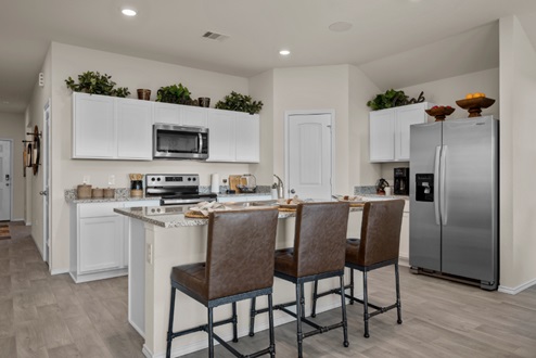 Rockbridge Model Home open-concept kitchen with white cabinetry, corner pantry, vinyl plank flooring, and view to front door.