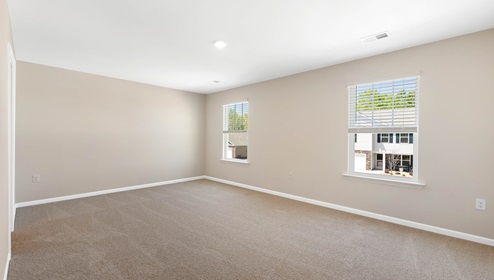 Primary bedroom with beige carpet and two large windows. New home in Asheville, North Carolina