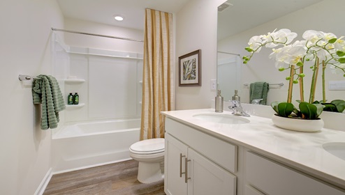 Bathroom with double sink vanity, white cabinets, and bathtub shower combination