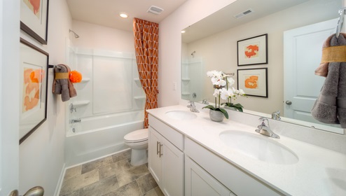 Bathroom with double sinks, white counters and cabinets, and bathtub