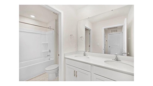 Bathroom with double sinks, bathtub, and white counters and cabinets