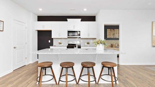 Kitchen and island with white cabinets, quarts countertops, wood floors, and stainless steel appliances