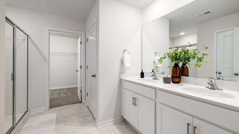 Primary bathroom with double sink vanity, white counter and cabinets, and glass door shower