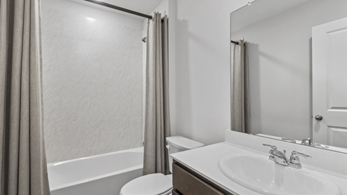 Secondary bathroom with hardwood floors light colored cabinets and white counters and tub
