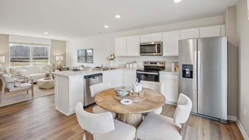 open concept first floor of home featuring a wooden dining table with 4 chairs, overlooking the kitchen with white cabinetry and stainless steel appliances