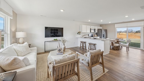 open concept living room with tan and white decor overlooking a TV on the back wall, overlooking the kitchen