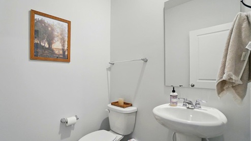 powder bathroom featuring a toilet, pedestal sink and mirror above
