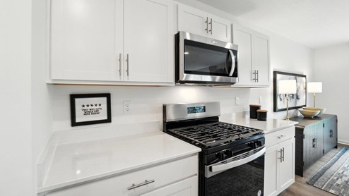 white cabinets, hard surface counters, stainless steel microwave, gas stove range